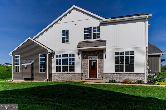 modern inspired farmhouse featuring a front lawn, stone siding, and a standing seam roof