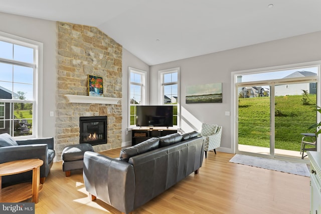living area featuring a stone fireplace, baseboards, light wood-style flooring, and lofted ceiling