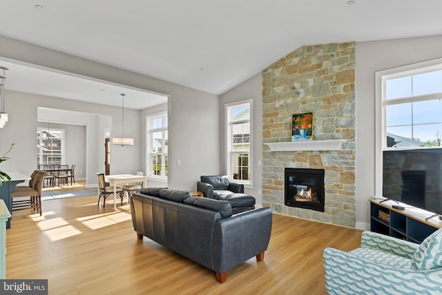 living room with plenty of natural light, light wood-style flooring, a chandelier, and a stone fireplace