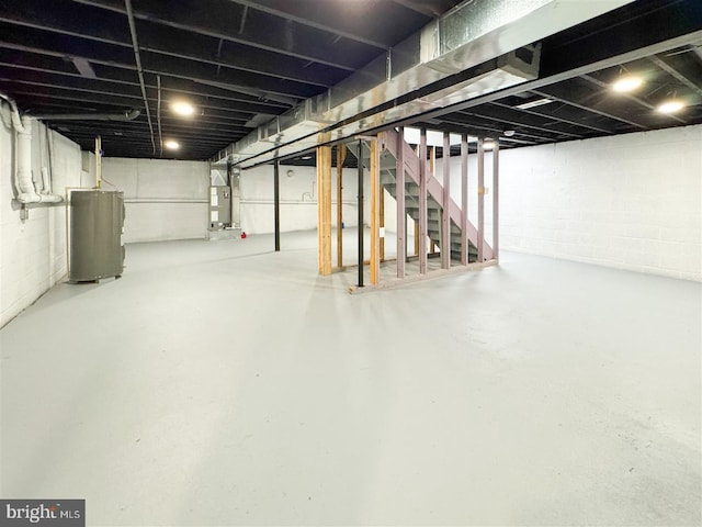 unfinished below grade area with stairs, water heater, and concrete block wall