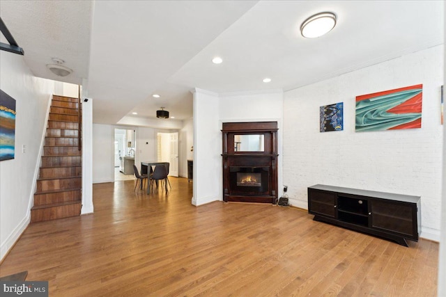 living area with light wood-style floors, stairs, a glass covered fireplace, baseboards, and recessed lighting