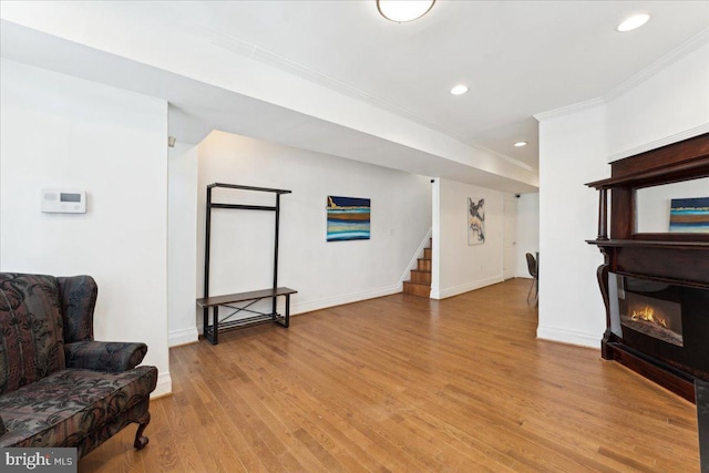sitting room featuring crown molding, stairs, wood finished floors, baseboards, and a glass covered fireplace