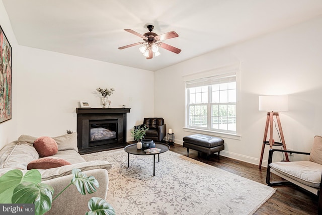 living room with baseboards, a ceiling fan, a glass covered fireplace, and wood finished floors