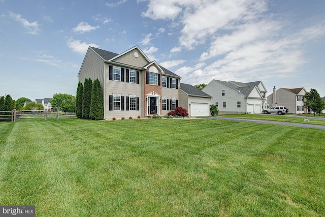 colonial home with a garage, fence, a front lawn, and aphalt driveway