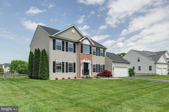 colonial house with a garage, fence, a front yard, and aphalt driveway