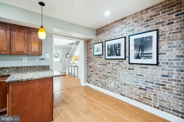 13446 Overbrook Ln, Bowie, MD 20715 - kitchen featuring brick wall, brown cabinetry, light wood-style flooring, dark stone counters, and hanging light fixtures