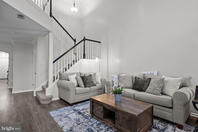 living room with ornamental molding, wood finished floors, stairway, and a towering ceiling