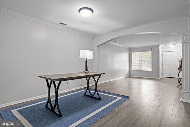 unfurnished office featuring arched walkways, baseboards, wood finished floors, visible vents, and ornamental molding