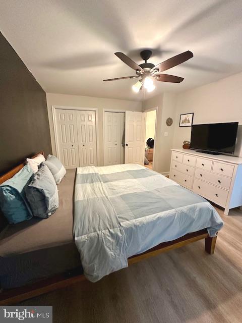 bedroom featuring a ceiling fan, two closets, and wood finished floors
