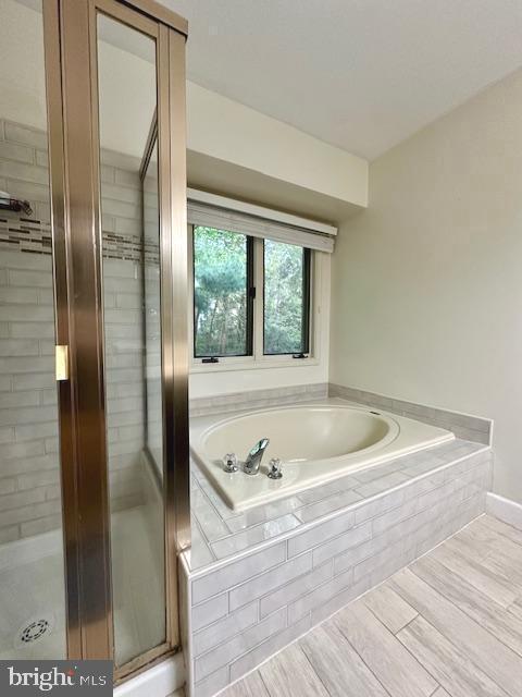 bathroom with a garden tub, wood finished floors, and a shower stall