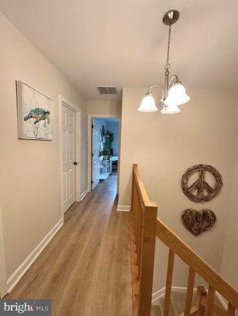 corridor featuring visible vents, wood finished floors, baseboards, a notable chandelier, and an upstairs landing
