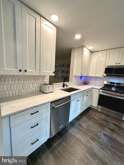 kitchen with white cabinets, tasteful backsplash, light stone counters, a sink, and appliances with stainless steel finishes