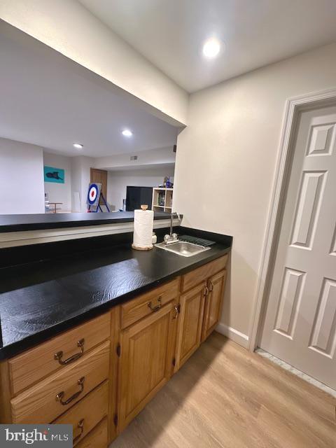 kitchen featuring brown cabinets, dark countertops, a sink, light wood-style floors, and recessed lighting