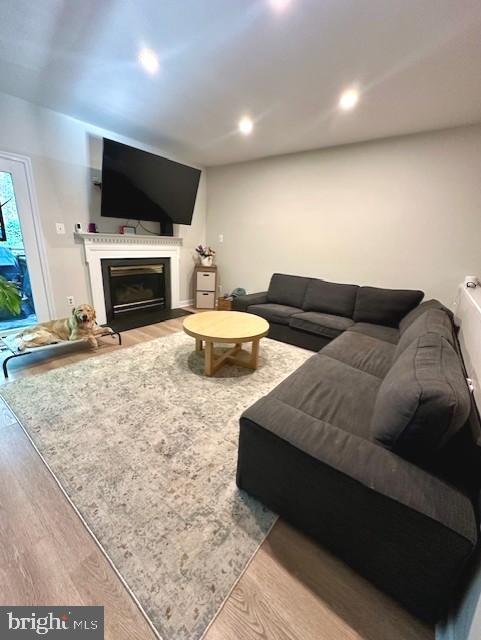 living room with recessed lighting, a glass covered fireplace, and wood finished floors