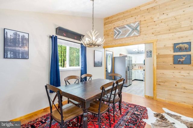 dining room featuring an inviting chandelier, light wood-type flooring, and wood walls