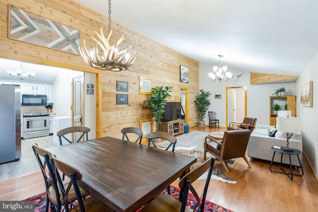dining room with wood walls, an accent wall, light wood-type flooring, a chandelier, and vaulted ceiling