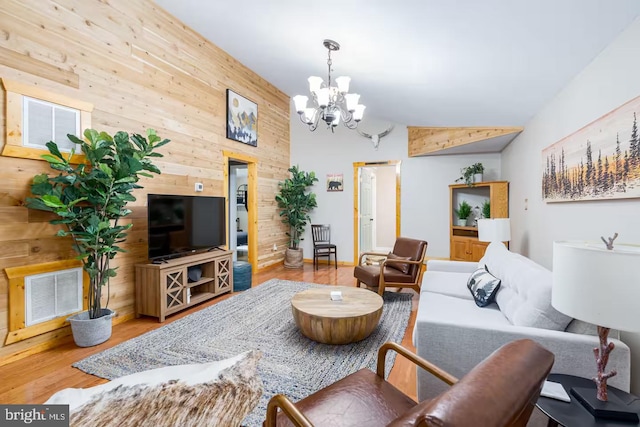 living room with visible vents, wood walls, lofted ceiling, wood finished floors, and a notable chandelier