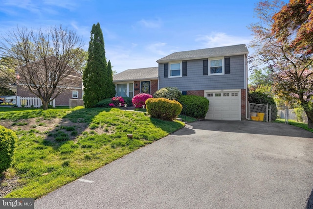 split level home featuring fence, an attached garage, brick siding, and aphalt driveway