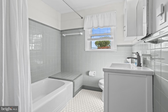 bathroom with tile walls, shower / bathtub combination with curtain, vanity, and toilet