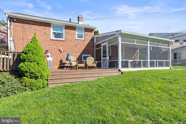 rear view of property featuring a deck, a chimney, a sunroom, brick siding, and a lawn