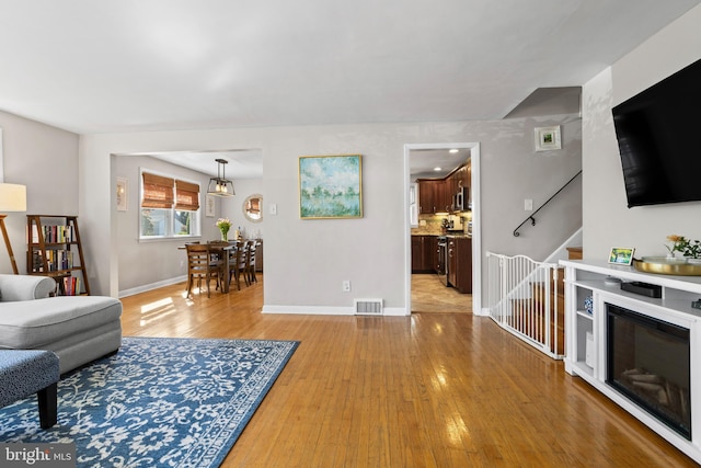 living room featuring stairway, baseboards, light wood-style flooring, and visible vents