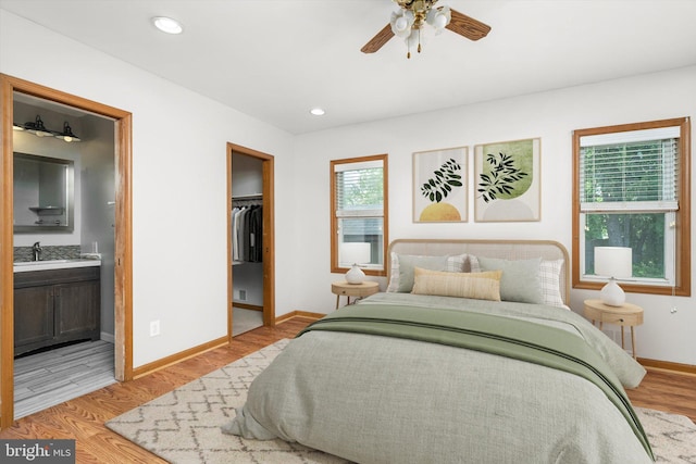 bedroom with baseboards, light wood-style floors, a spacious closet, a sink, and ensuite bath