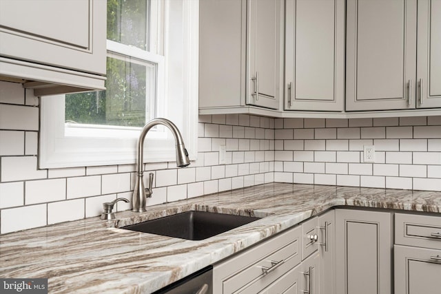 kitchen with gray cabinets, light stone counters, a sink, and tasteful backsplash