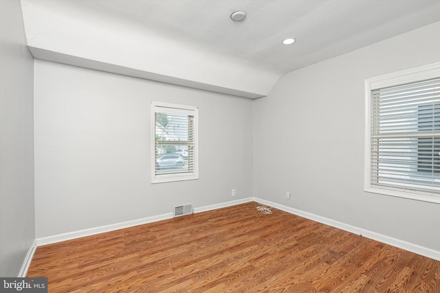 unfurnished room featuring visible vents, baseboards, wood finished floors, and vaulted ceiling