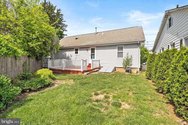rear view of property with a lawn, roof with shingles, a wooden deck, and fence