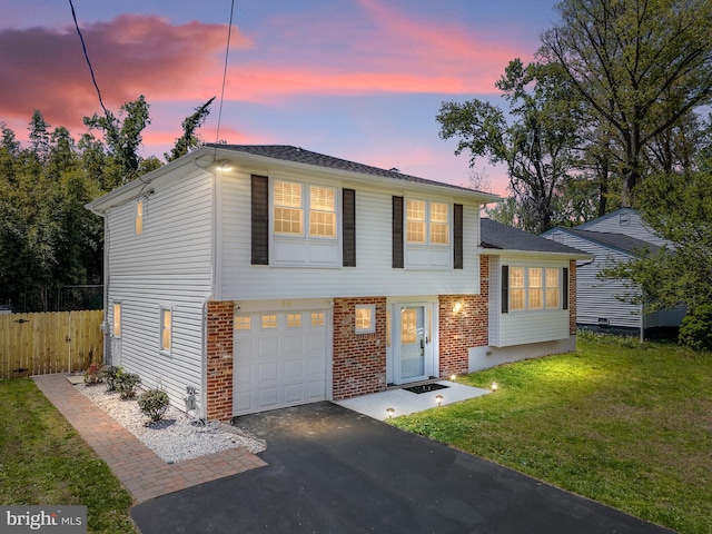 tri-level home featuring a front lawn, aphalt driveway, fence, brick siding, and an attached garage
