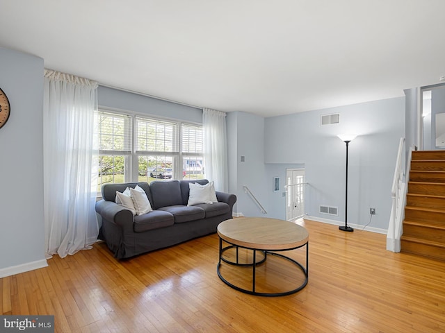 living room featuring visible vents, baseboards, light wood finished floors, and stairs