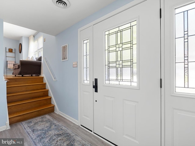 foyer entrance with baseboards, visible vents, wood finished floors, and stairway