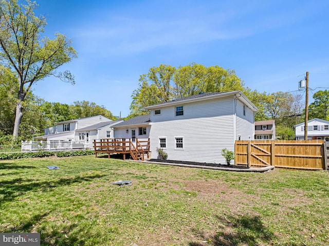 rear view of house with fence, a wooden deck, and a yard