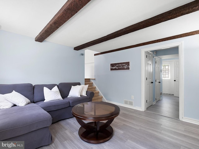 living area with baseboards, visible vents, wood finished floors, and beam ceiling