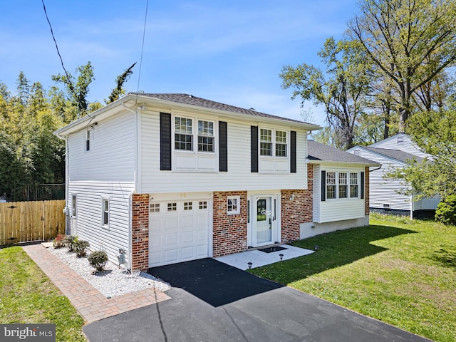 tri-level home with driveway, a garage, brick siding, fence, and a front lawn