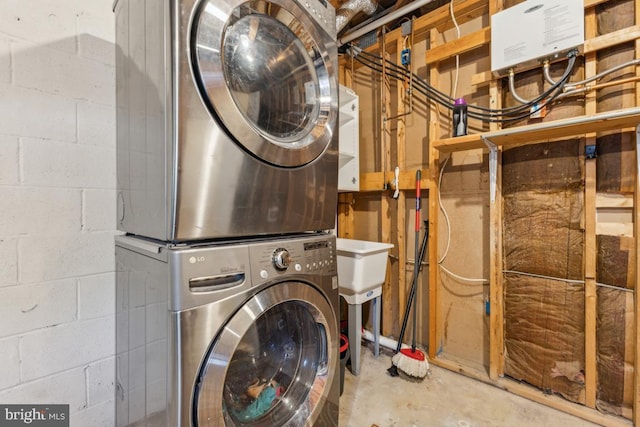 laundry area with laundry area, stacked washer / drying machine, and concrete block wall