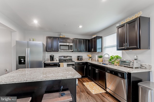 kitchen with appliances with stainless steel finishes, dark wood-style floors, a sink, light stone counters, and recessed lighting