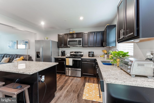 kitchen featuring appliances with stainless steel finishes, a sink, dark wood-style flooring, light stone counters, and a kitchen bar