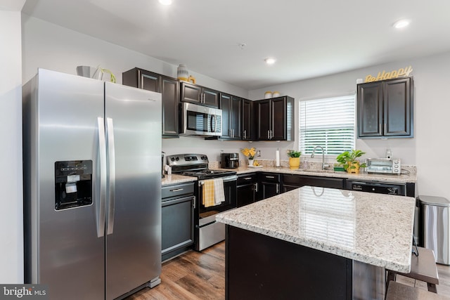 kitchen featuring stainless steel appliances, a sink, light stone counters, wood finished floors, and recessed lighting