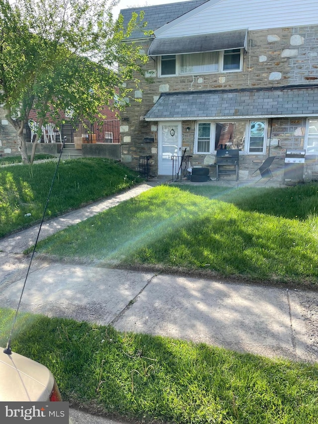 townhome / multi-family property with a front lawn, a high end roof, and stone siding