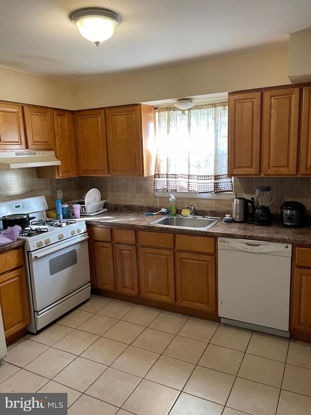 kitchen with a sink, brown cabinetry, under cabinet range hood, and white appliances