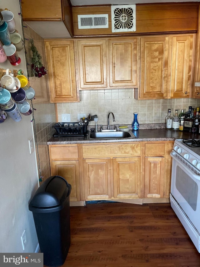 kitchen with backsplash, dark countertops, white gas range oven, and a sink