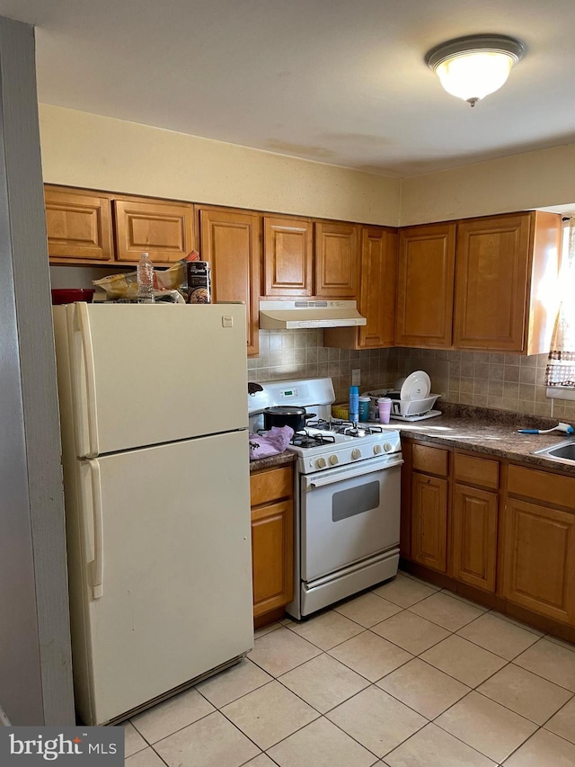 kitchen featuring brown cabinetry, under cabinet range hood, and white appliances