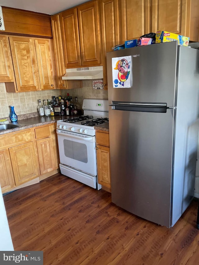 kitchen featuring white gas range, decorative backsplash, dark wood-style flooring, freestanding refrigerator, and under cabinet range hood