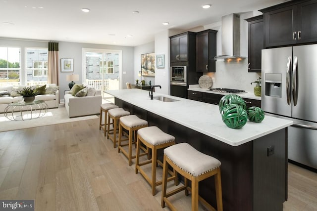 kitchen with stainless steel appliances, open floor plan, a sink, and wall chimney exhaust hood
