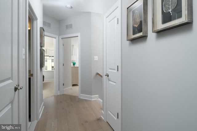 hall featuring baseboards, visible vents, and light wood-type flooring