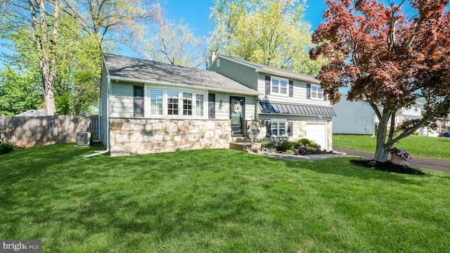 tri-level home featuring a garage, a front lawn, fence, stone siding, and central air condition unit
