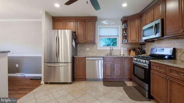 kitchen featuring ceiling fan, light stone counters, a sink, backsplash, and stainless steel appliances