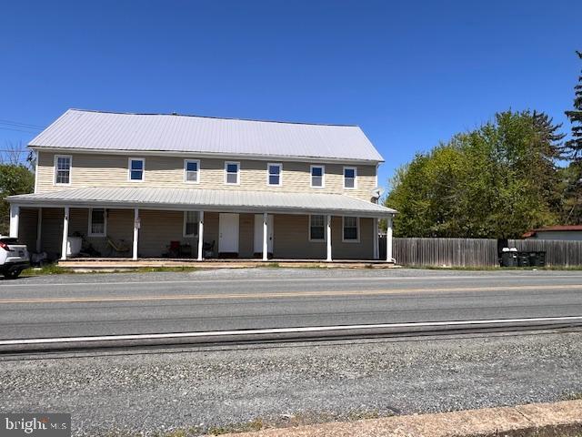 farmhouse-style home with covered porch, fence, and metal roof