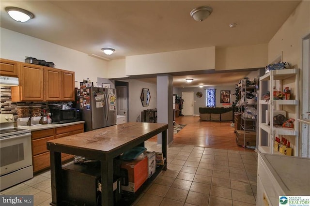 kitchen with freestanding refrigerator, under cabinet range hood, electric range, and light tile patterned flooring